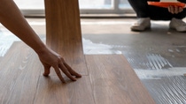 Close-up of hands installing brown wood-like flooring in a sunlit room. Close-up of hands installing brown wood-like flooring in a sunlit room.